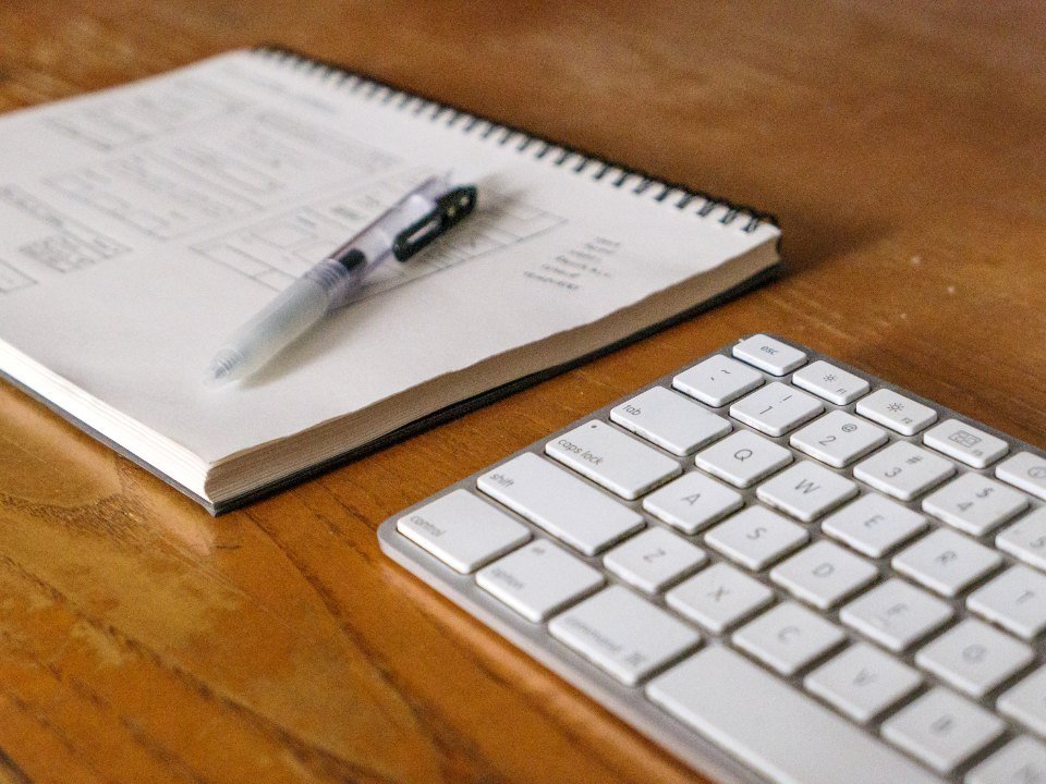 Cuaderno con una pluma encima junto a un teclado de computadora