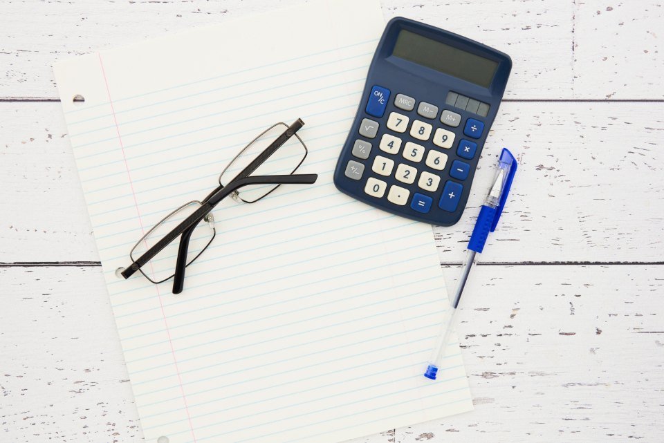 Calculadora, anteojos y una hoja con anotaciones sobre una mesa blanca