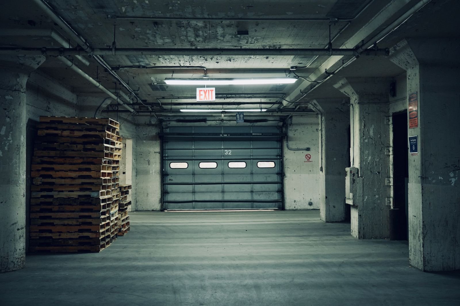 Interior de una bodega industrial vacía con tarimas apiladas y cortina metálica cerrada
