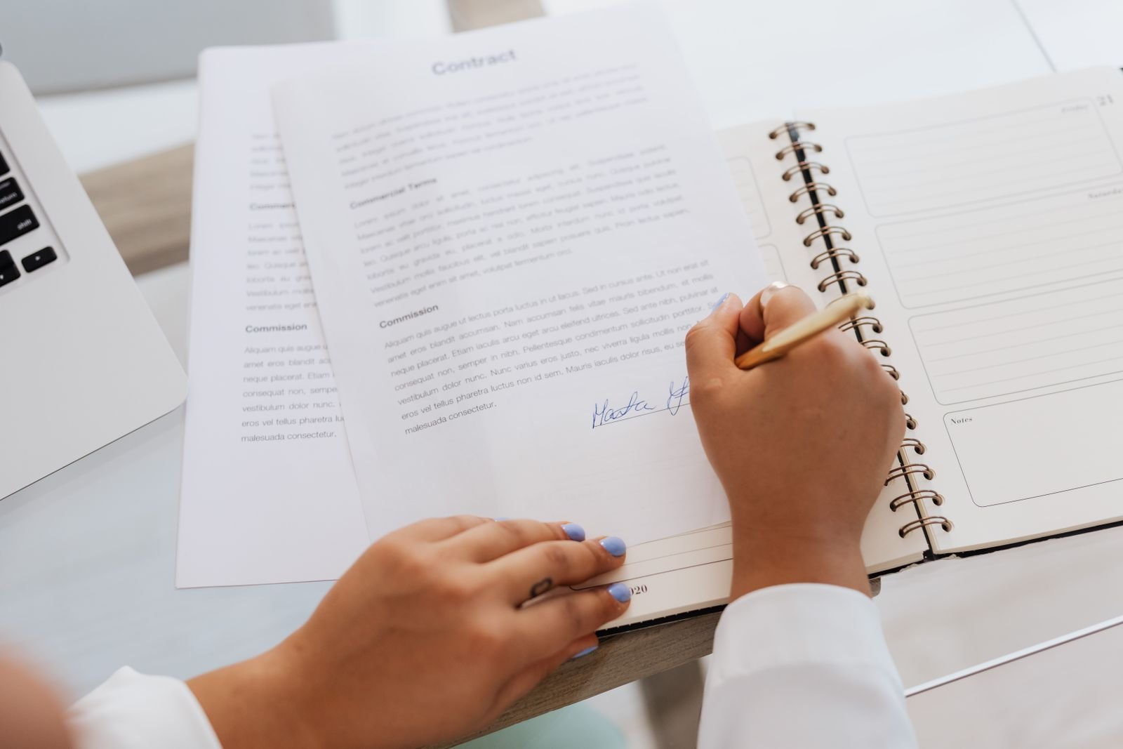 Manos firmando un contrato sobre un escritorio con artículos de oficina