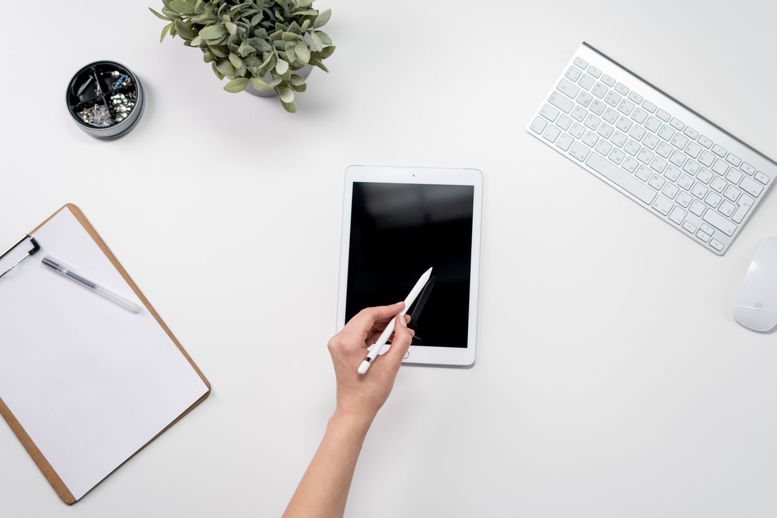 Escritorio minimalista con tableta, lápiz digital, teclado y artículos de oficina