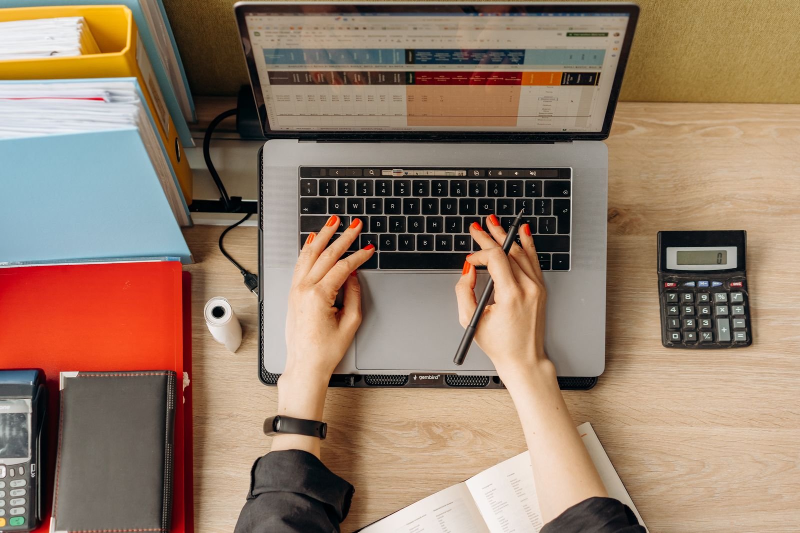 Vista cenital de manos trabajando en una laptop sobre un escritorio con carpetas y una calculadora