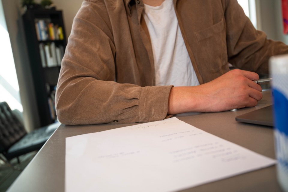 Persona escribiendo notas a mano sobre una hoja en blanco en un escritorio