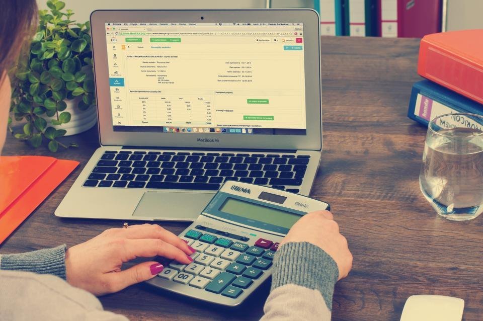 Manos usando una calculadora frente a una laptop con una hoja de cálculo