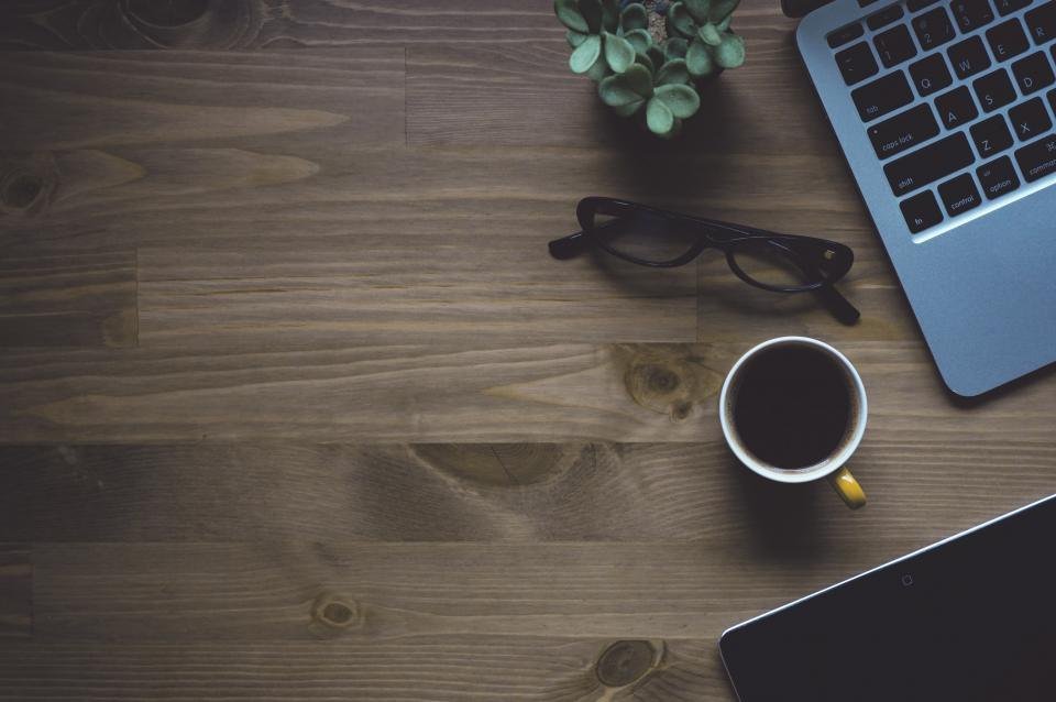 Laptop abierta, anteojos y taza de café sobre un escritorio de madera